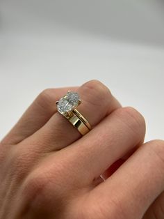 a woman's hand holding a yellow gold ring with a diamond on it and a white background