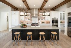 a large kitchen with three stools in front of the island and two ovens