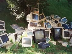 a pile of old computer monitors sitting on top of a grass covered field next to a tree