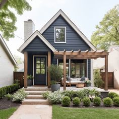 a small blue house with a covered porch and pergolated garden in the front yard