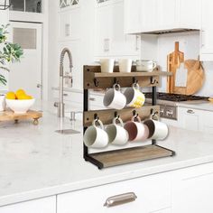 a kitchen with white cabinets and marble countertops has mugs hanging on the rack