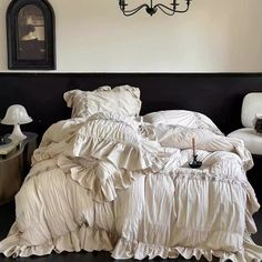 an unmade bed with white sheets and ruffled bedspread in front of a chandelier