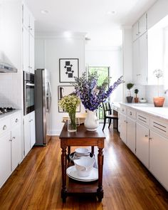 a kitchen with white cabinets and wooden flooring has flowers in a vase on the island