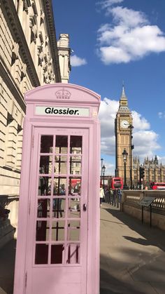 a pink phone booth stands in front of the big ben clock tower