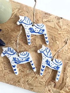 three blue and white ceramic horse ornaments on a wooden board with string hanging from it