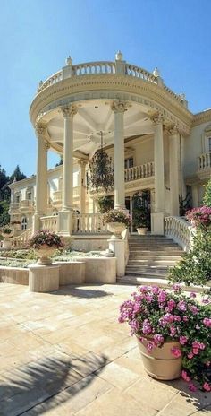 a large white house with lots of flowers in the front yard and stairs leading up to it