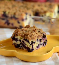 a piece of blueberry crumb cake on a yellow plate next to a serving dish