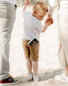 a little boy standing next to his parents feet on the beach while they hold hands