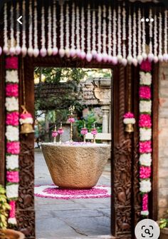 an outdoor fountain decorated with pink and white flowers is seen through the doorway to a garden