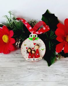 a christmas ornament with red flowers and pine cones in the background on a wooden table