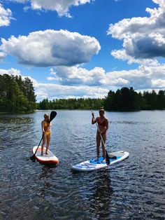 two people on paddle boards paddling in the water with trees and clouds behind them