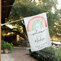 a welcome baby sign hanging from a clothes line in front of a house with a rainbow painted on it