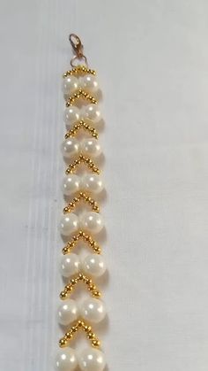 a gold and white beaded bracelet with pearls on it's end, hanging from a chain