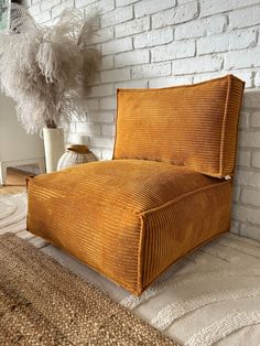 an orange couch sitting on top of a rug next to a white vase with feathers