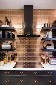 a kitchen with black cabinets and brown brick backsplashing, stainless steel range hood