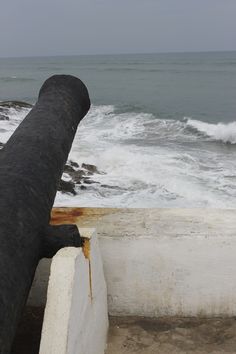 an old pipe on the edge of a wall near the ocean with waves crashing in