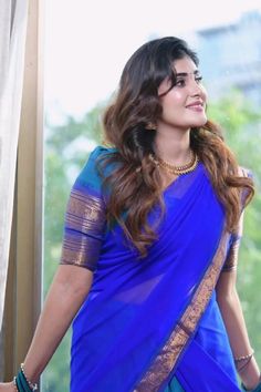 a woman in a blue sari is standing by a window with her hands on her hips