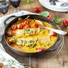 a skillet filled with food on top of a wooden table next to tomatoes and other vegetables