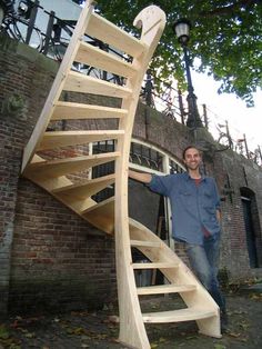 a man standing in front of a wooden spiral staircase next to a brick wall and lamp post