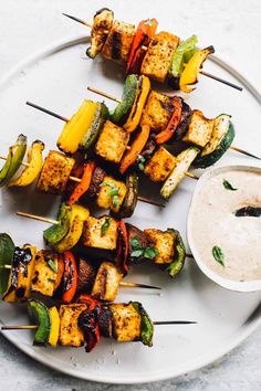 several skewers of food on a plate with dipping sauce