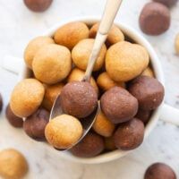 a bowl filled with chocolate covered donuts on top of a white counter next to spoons