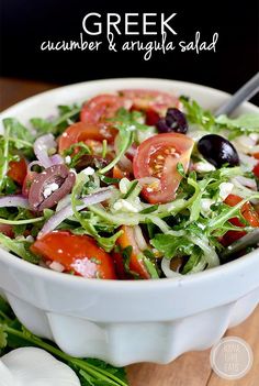 a salad in a white bowl with olives, tomatoes and lettuce on the side