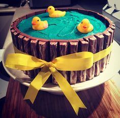 a cake decorated with rubber ducks on top of a wooden table next to a yellow ribbon