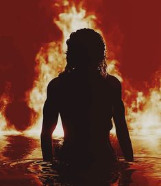 a woman standing in the water with fire behind her