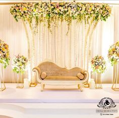 a couch sitting in front of a white stage with flowers on it and gold stands