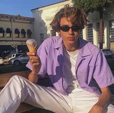 a young man sitting on a bench holding an ice cream cone in his right hand