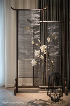 a vase with flowers in it sitting next to a curtained window and a birdcage