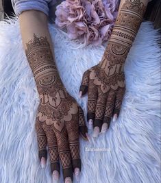 two hands with henna tattoos on them sitting on a fluffy white rug next to a flower