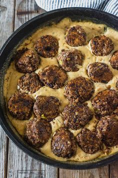 a skillet filled with meatballs and gravy on top of a wooden table