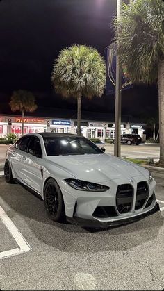 a white sports car parked in a parking lot next to palm trees and gas pumps