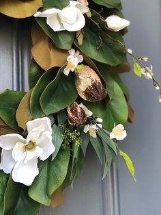 a wreath with white flowers and green leaves hanging on a gray door frame, ready to be decorated