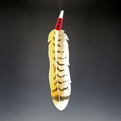 a yellow and white feather ornament hanging from a string on a black background