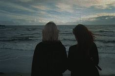 two women standing on the beach looking out at the ocean