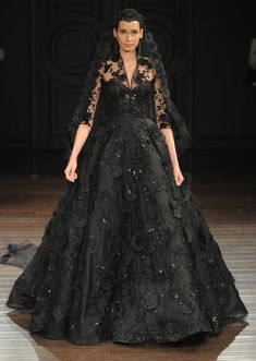 a woman in a black dress on the runway at a fashion show, wearing an elaborately designed gown