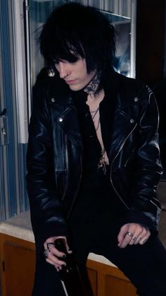 a man with black hair and piercings sitting on top of a counter next to a window