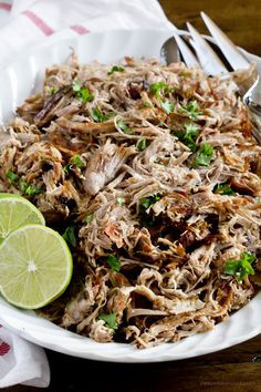 a white bowl filled with shredded meat and garnished with cilantro next to a lime wedge