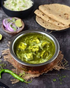 a metal bowl filled with green curry next to pita bread