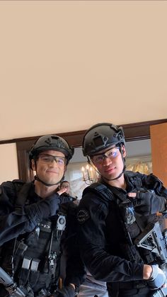 two men wearing helmets and goggles standing next to each other in front of a mirror