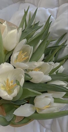 a bouquet of white tulips and green leaves on top of a bed sheet