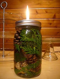 a mason jar filled with pine cones and green moss sits on a table next to a candle