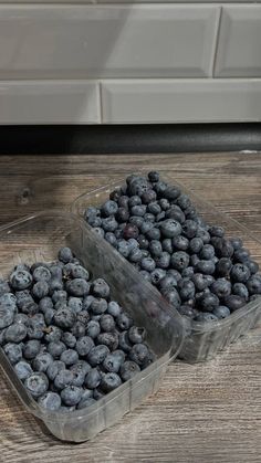 two plastic containers filled with blueberries on top of a wooden table