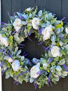 a wreath with white flowers and greenery hanging on a door