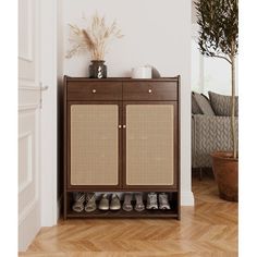 a wooden cabinet with shoes on it in front of a couch and potted plant