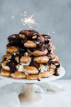 a stack of doughnuts covered in chocolate and sprinkles with a sparkler on top