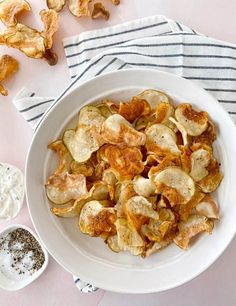 a white bowl filled with potato chips next to two spoons and a striped napkin