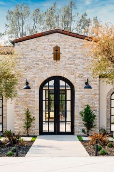 the front entrance to a home with black doors and windows, surrounded by stone walls